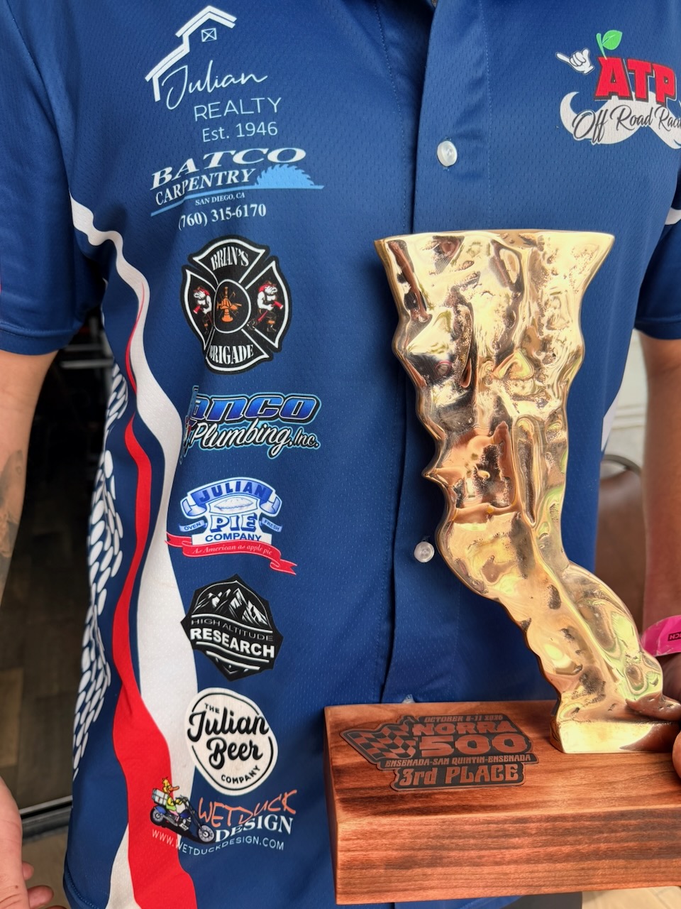 The 2026 NORRA 500 third-place trophy displayed beside the team’s sponsor logos
